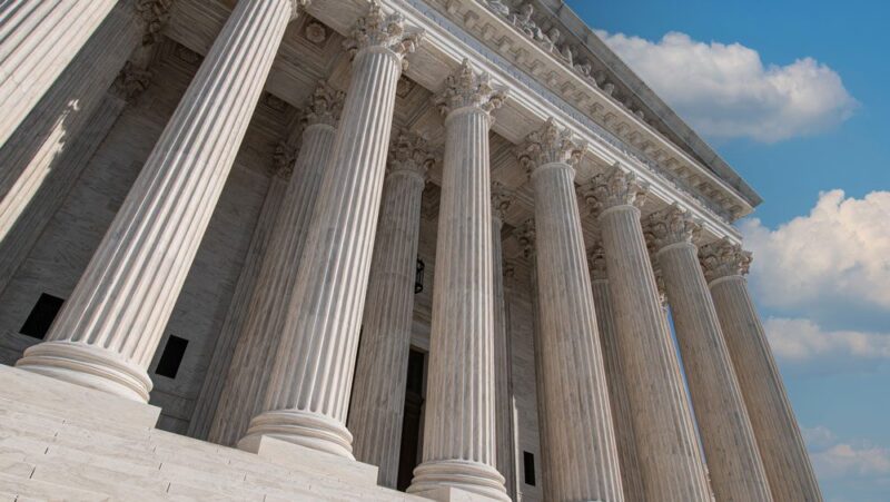 An image of the exterior of a courthouse against a blue sky with clouds